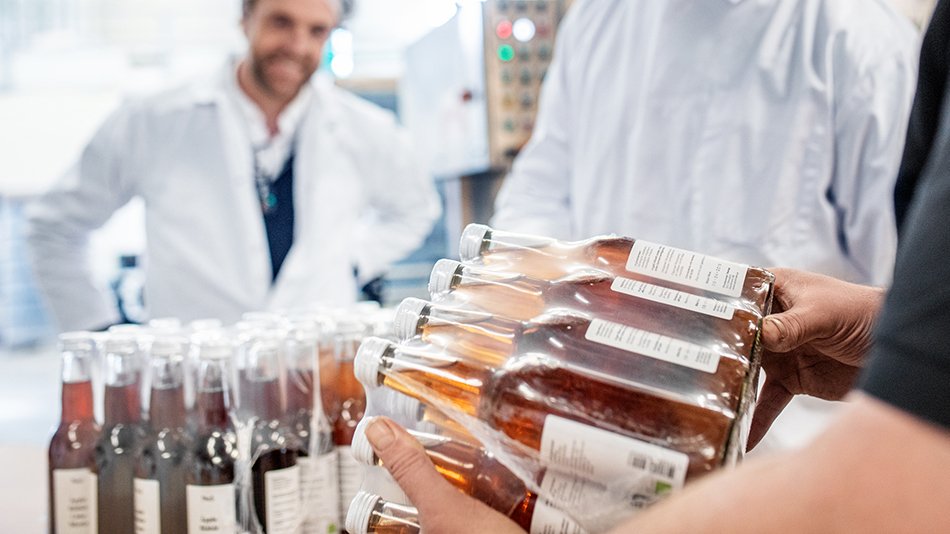 Three persons looking at bottles with apple juice